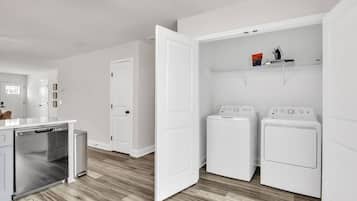 A laundry room with a dishwasher, two stacked washers, and a shelf with cleaning supplies.