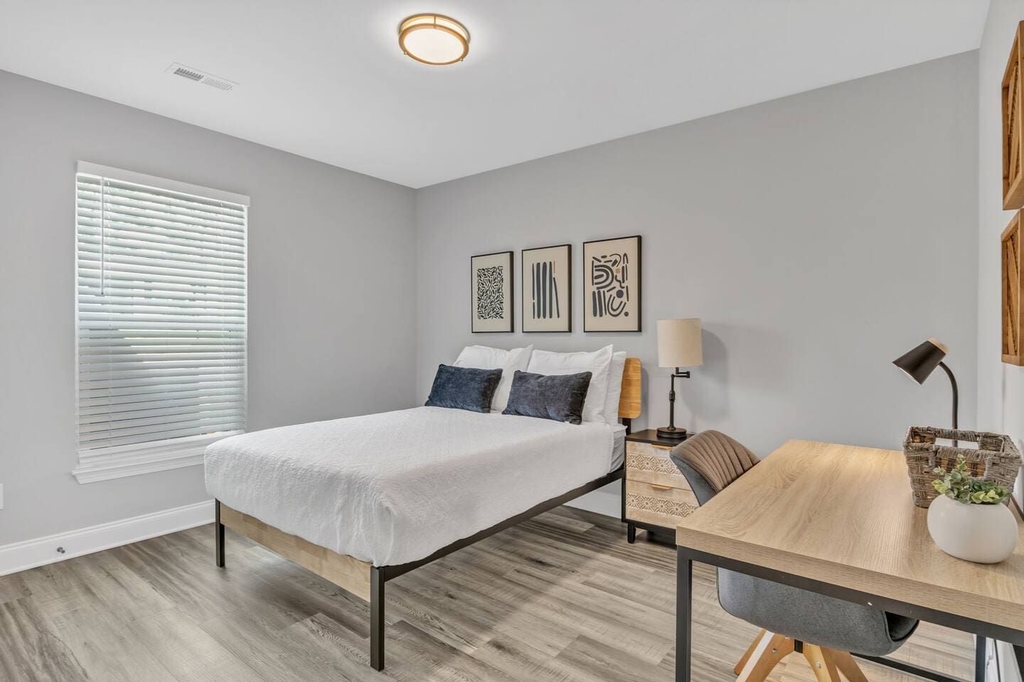 Un dormitorio moderno con cama, mesita de noche, lámpara y una obra de arte en la pared.