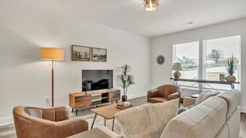 A modern living room with a flat-screen TV, leather armchairs, a sofa, a coffee table, and a floor lamp.