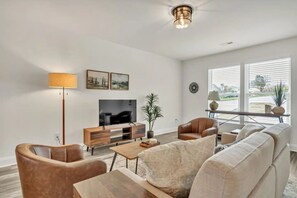 Una sala de estar moderna con un televisor de pantalla plana, sillones de cuero, un sofá, una mesa de centro y una lámpara de pie.