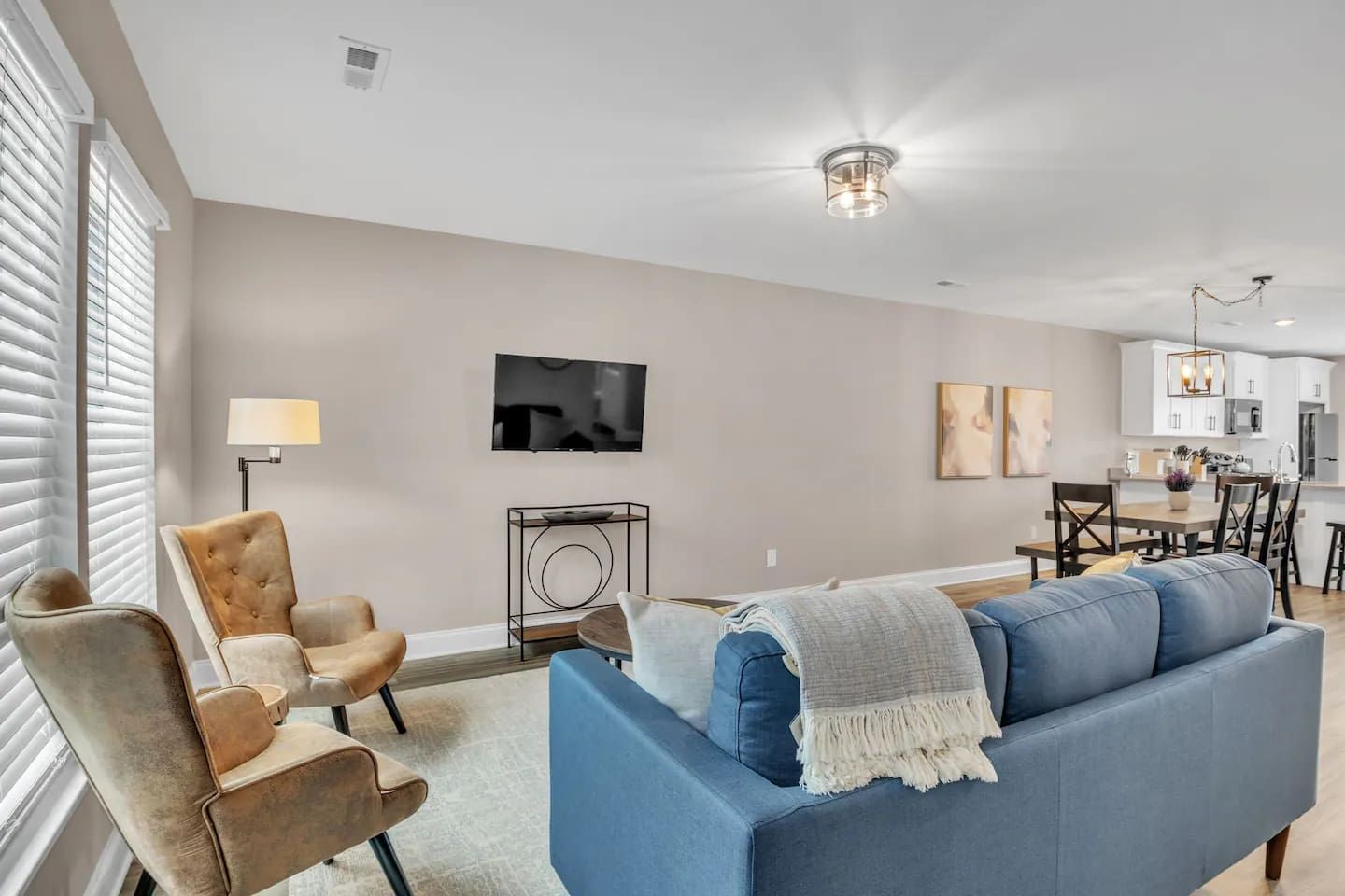 A modern living room with a blue sofa, a brown armchair, a TV, and a dining area with a table and chairs.