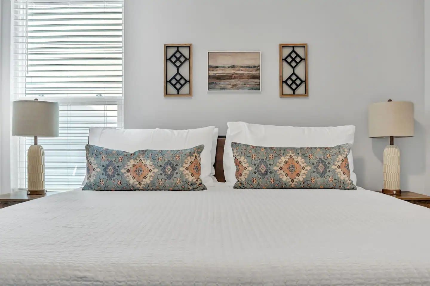 A hotel room with a large bed, two decorative pillows, a nightstand with a lamp, and two wall-mounted pictures.