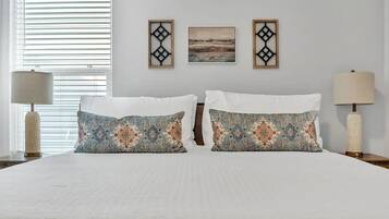 A hotel room with a large bed, two decorative pillows, a nightstand with a lamp, and two wall-mounted pictures.