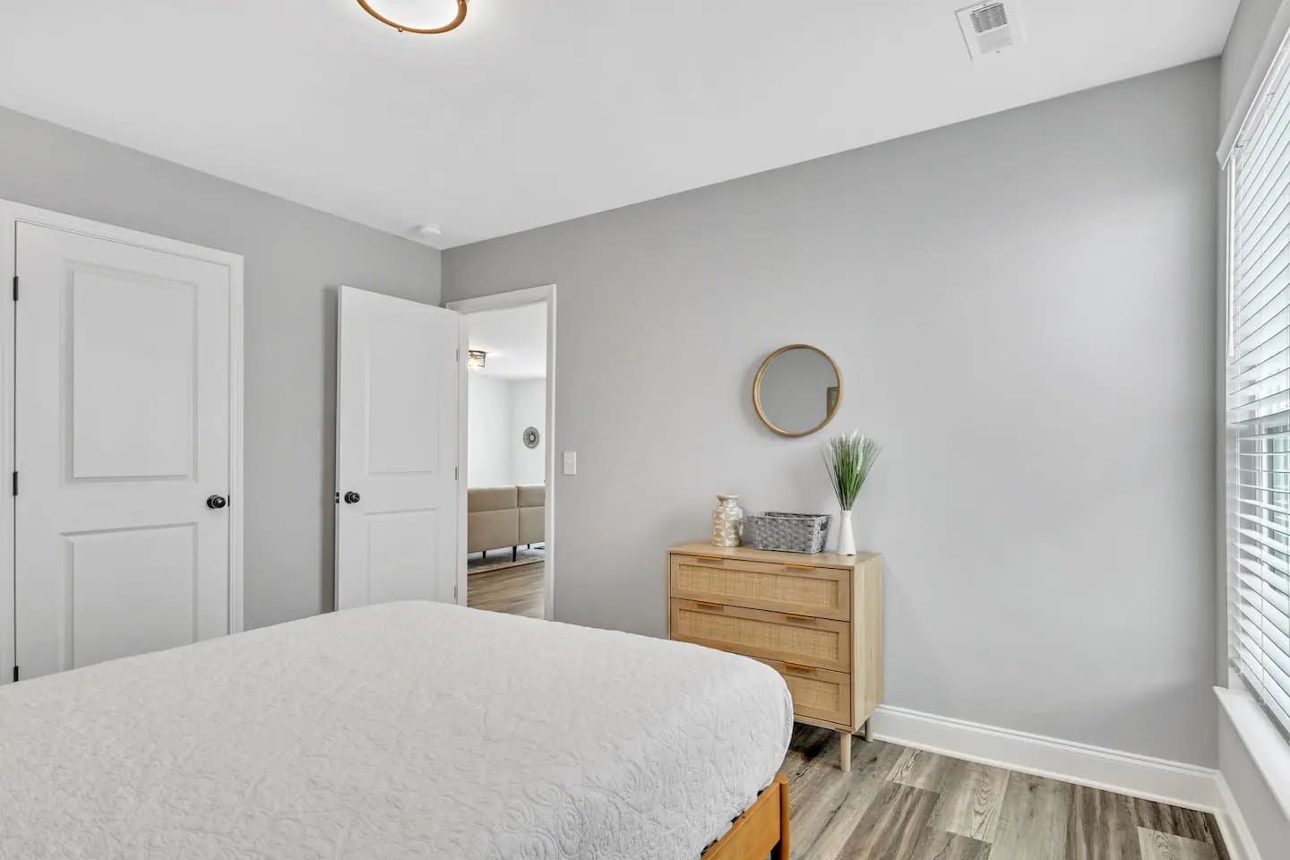 A bedroom with a bed, a dresser, a mirror, and a door leading to another room.