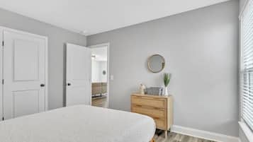 A bedroom with a bed, a dresser, a mirror, and a door leading to another room.