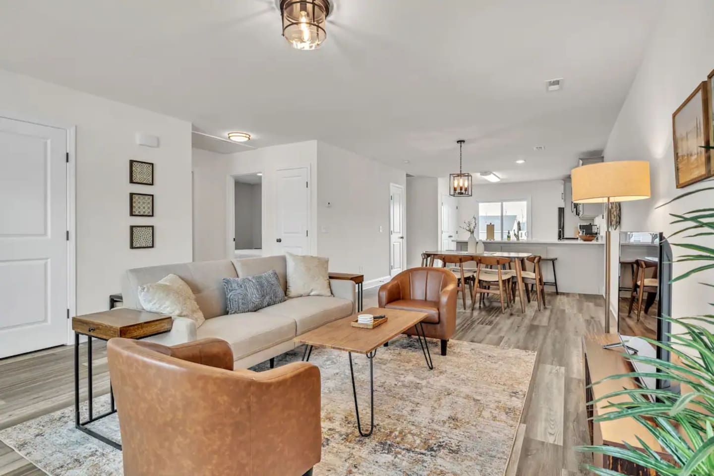 A spacious living area with a sofa, coffee table, and chairs, a dining area with a table and chairs, and a kitchen in the background.