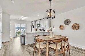 Una cocina moderna con armarios blancos, una mesa de comedor de madera con sillas y una lámpara colgante.