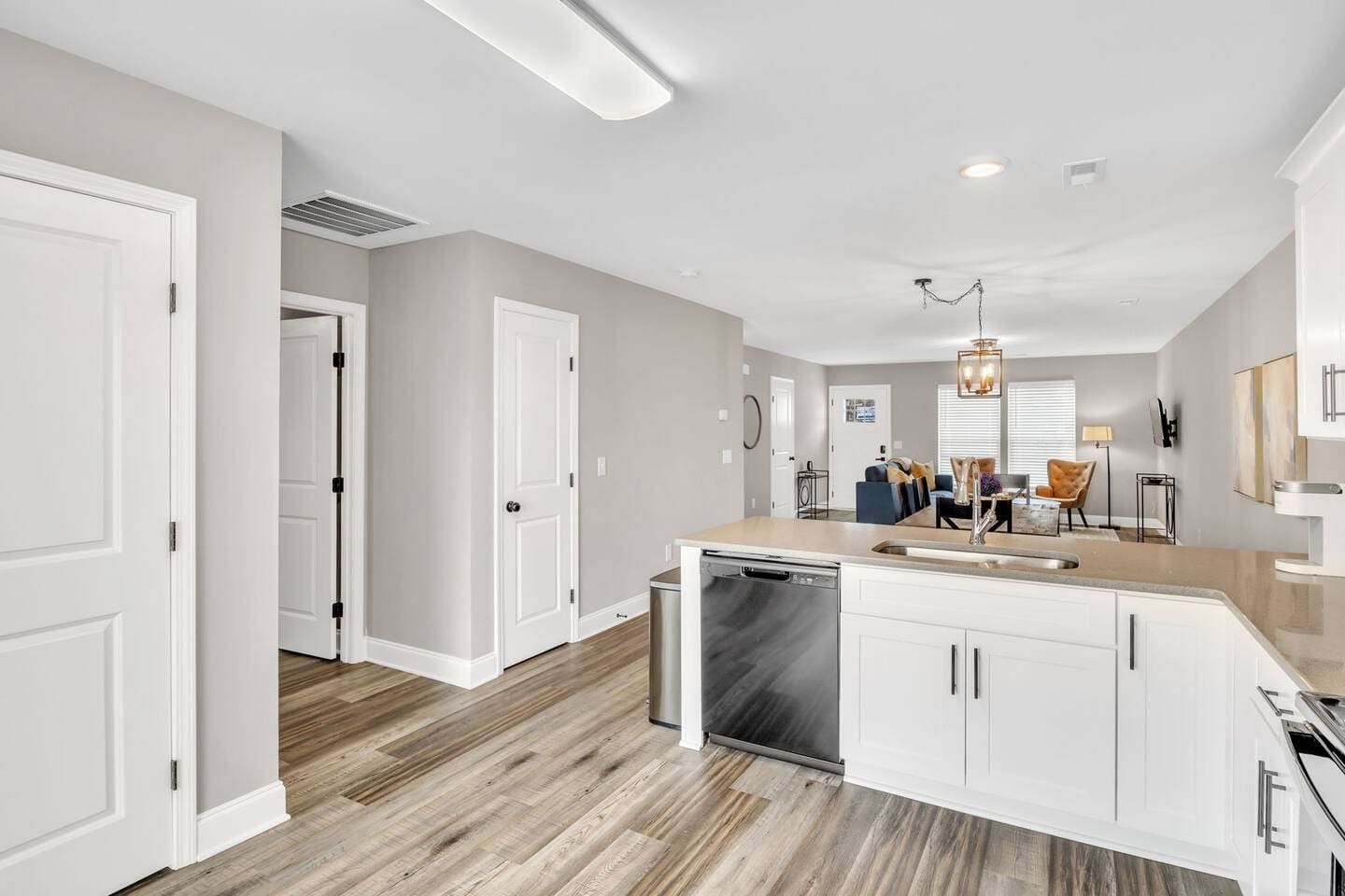 A modern kitchen with white cabinetry, a dishwasher, and a dining area with a blue sofa and orange chair.