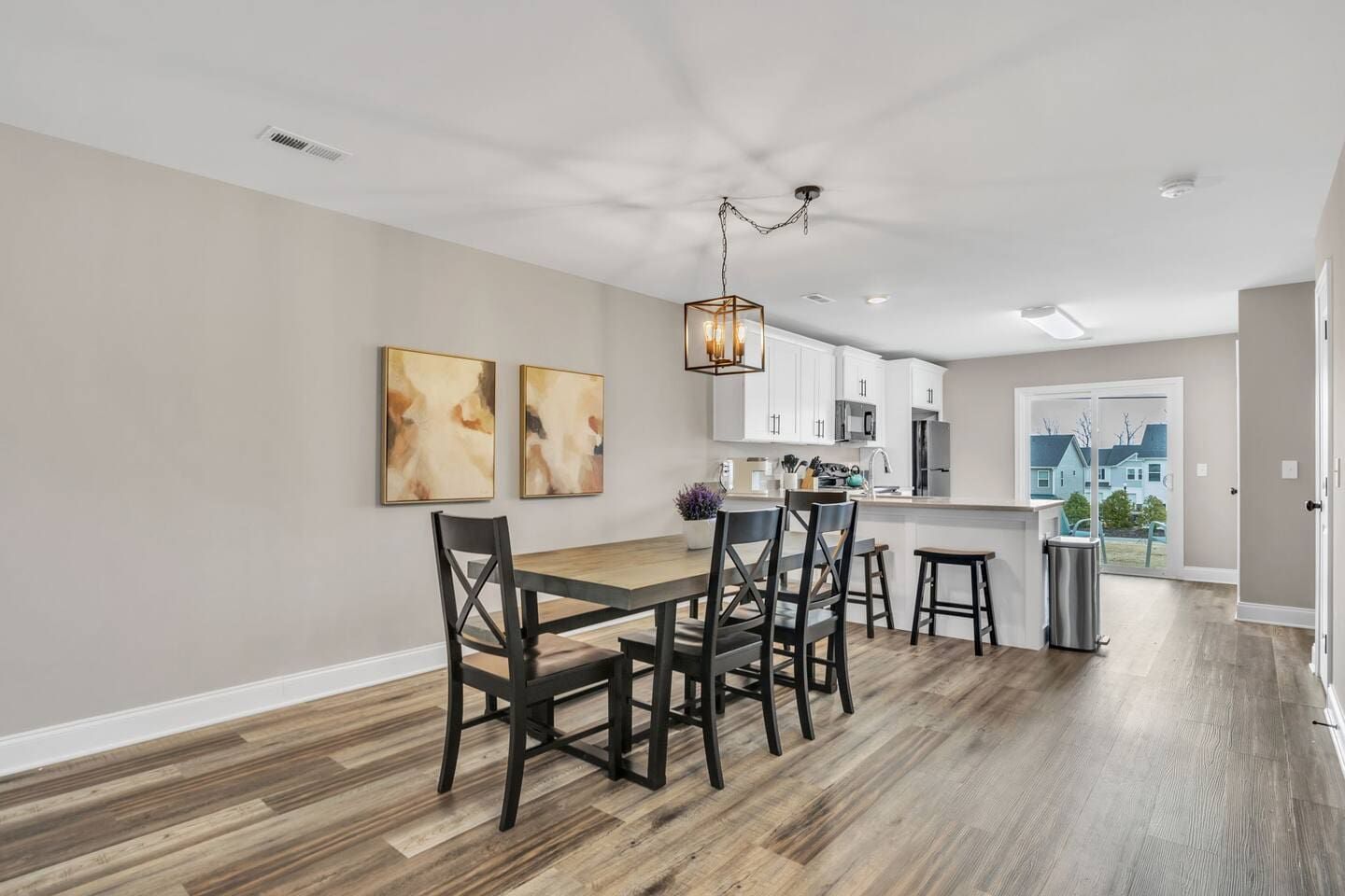 A modern kitchen with white cabinets, a wooden dining table, and a hanging light fixture.