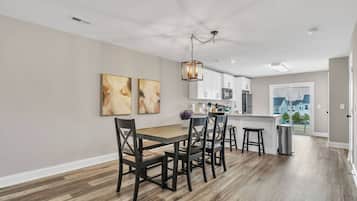 A modern kitchen with white cabinets, a wooden dining table, and a hanging light fixture.