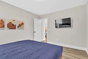 Un dormitorio con cama, puerta y televisor en la pared.