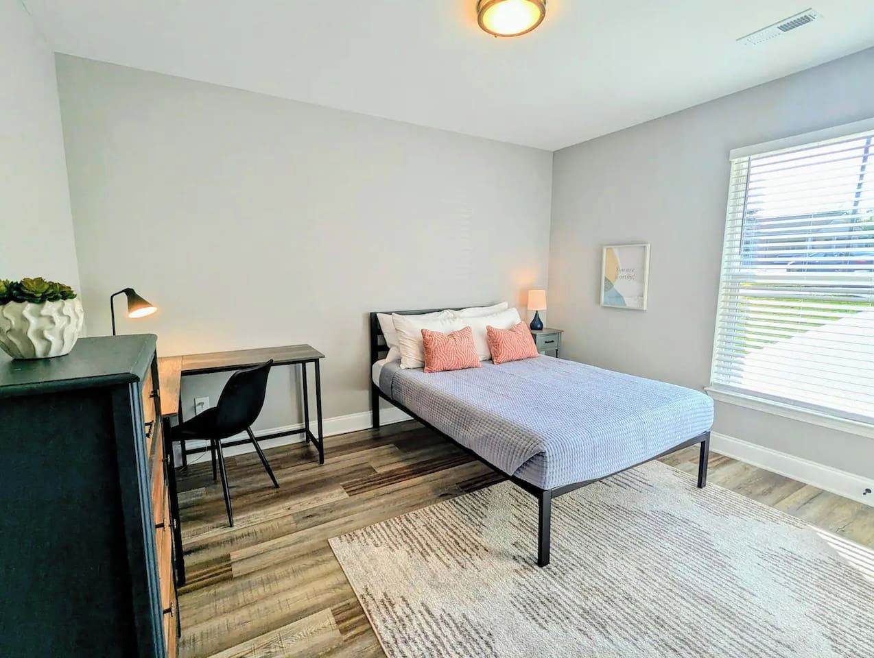 Un dormitorio con cama, mesita de noche, silla, escritorio y ventana con persianas.