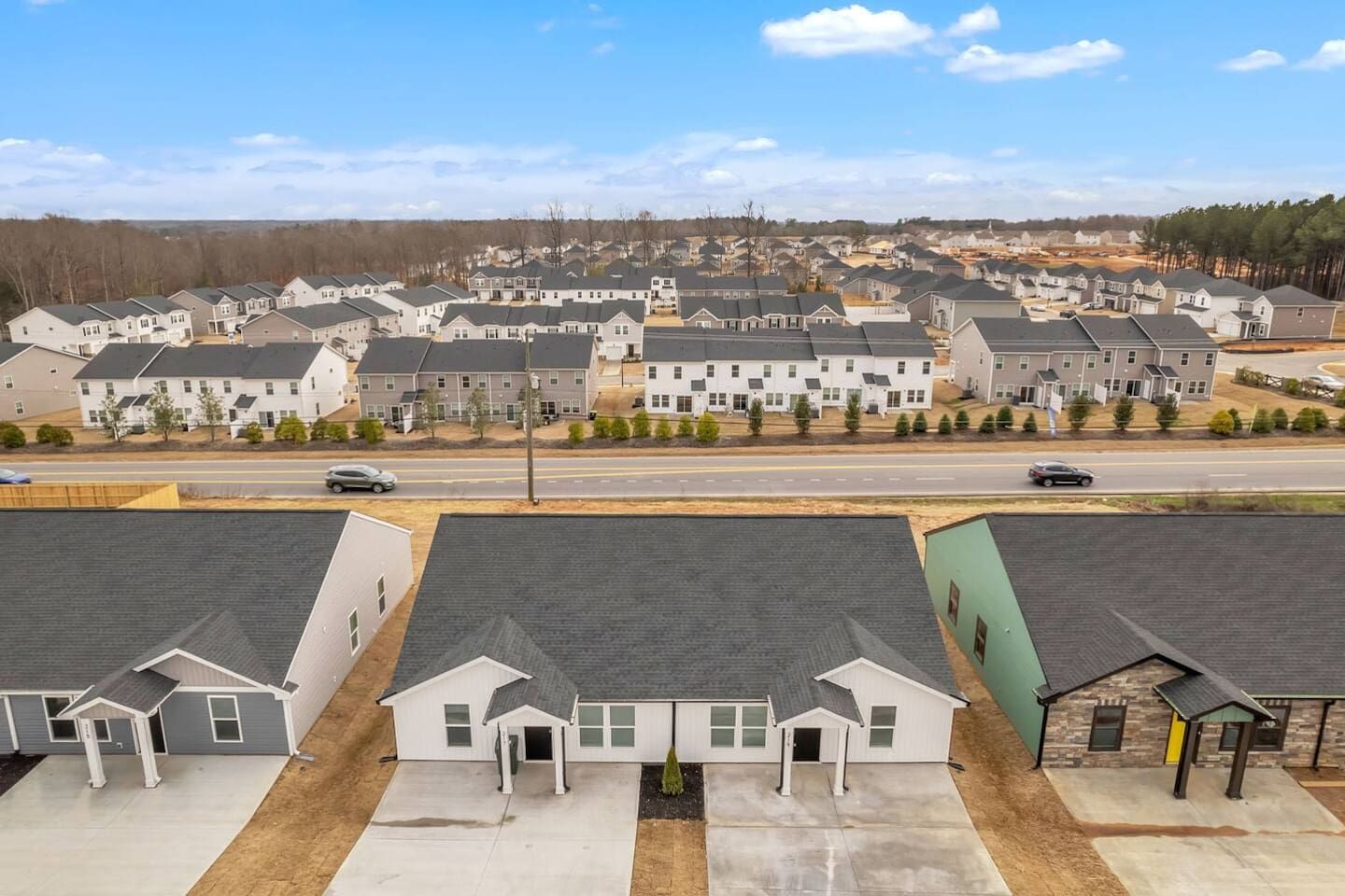 A residential area with multiple two-story houses, a main road, and a clear sky.
