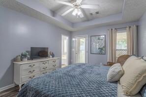 A bedroom with a bed, dresser, ceiling fan, and a door leading to another room.