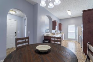 A spacious kitchen with a dining area, featuring a round wooden table, dark wooden chairs, and a white bowl.