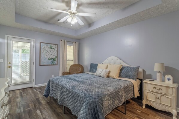 A bedroom with a bed, a nightstand, a lamp, a ceiling fan, and a window with blinds.