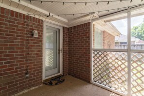 A room with a brick wall, a door with a glass panel, a wooden ceiling, and a lattice screen door.