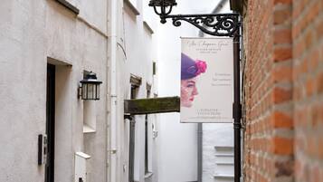 A narrow alley with a sign for 'Au Chateau Gris' boutique, a white building with a brick wall, and a hanging street lamp.