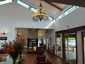 A spacious lobby with a high ceiling, a chandelier, seating area, and large windows.