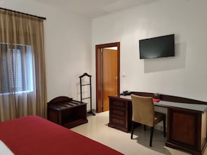 A hotel room with a bed, a desk, a chair, a television, and a wardrobe.