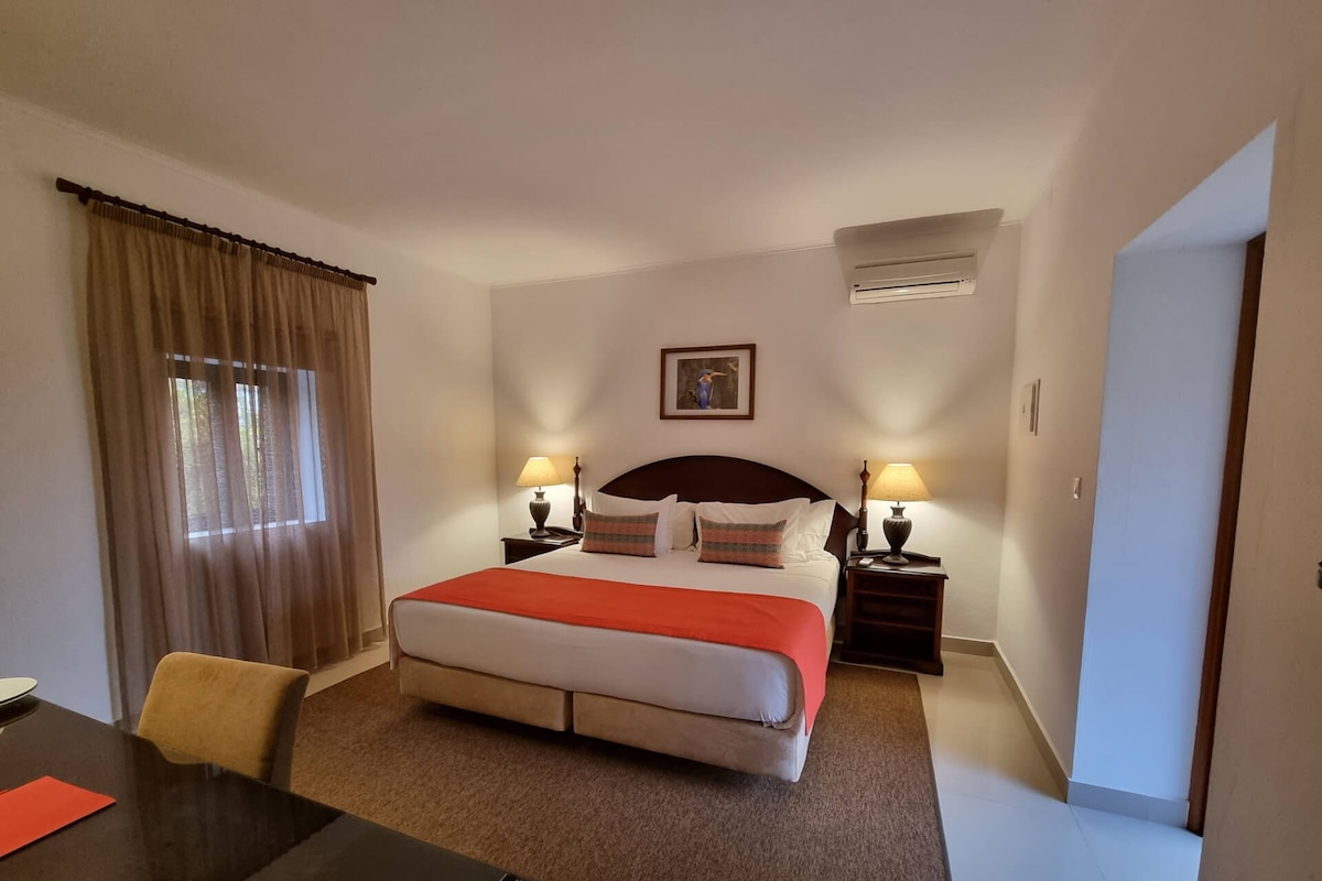 Hotellihuone, jossa on sänky, kaksi yöpöytää, työpöytä ja tuoli.