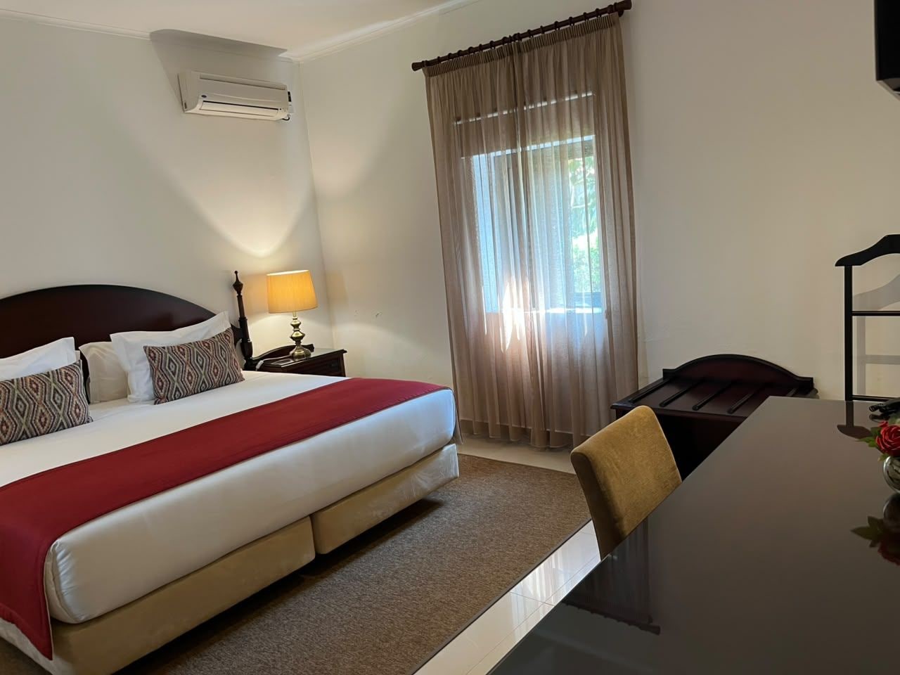 A hotel room with a bed, bedside table, lamp, and a desk with a chair.