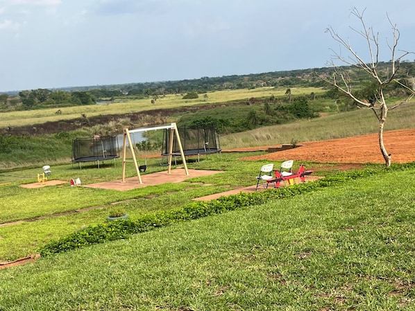 A grassy outdoor area with a swing set, exercise equipment, and a seating area with chairs.