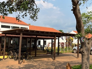 A covered outdoor area with a vehicle and a building with a red-tiled roof.