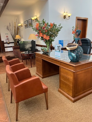 Zona d'estació amb un taulell de fusta, cadires de pell, televisió, llums penjades a la paret i objectes decoratius, incloent un vas amb flors i una cistella tradicional.
