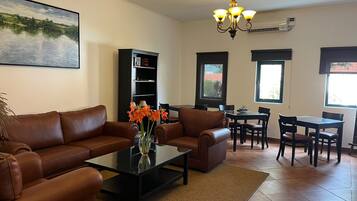 A living room with a sofa, coffee table, and a bookshelf. There is a dining area with a table and chairs.