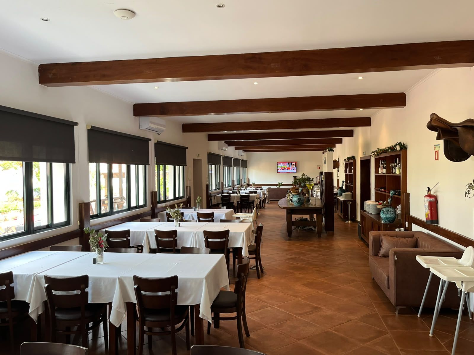 Un restaurant doté de nombreuses tables et chaises, de poutres en bois au plafond et d’un téléviseur fixé au mur.
