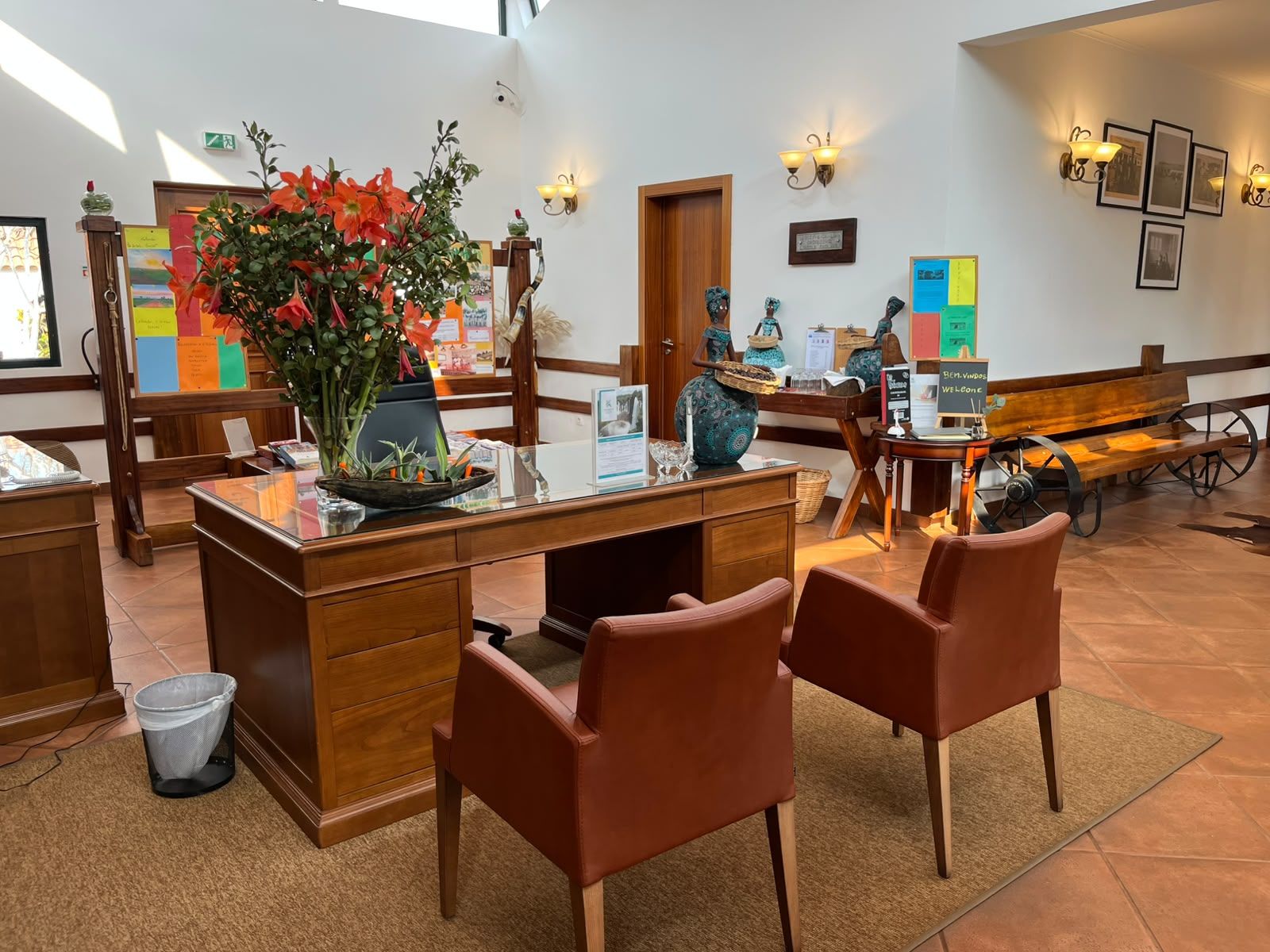 Un comptoir d’accueil orné d’un vase de fleurs, deux fauteuils en cuir marron, un banc en bois et un mur décoré de tableaux encadrés et d’un panneau d’affichage.
