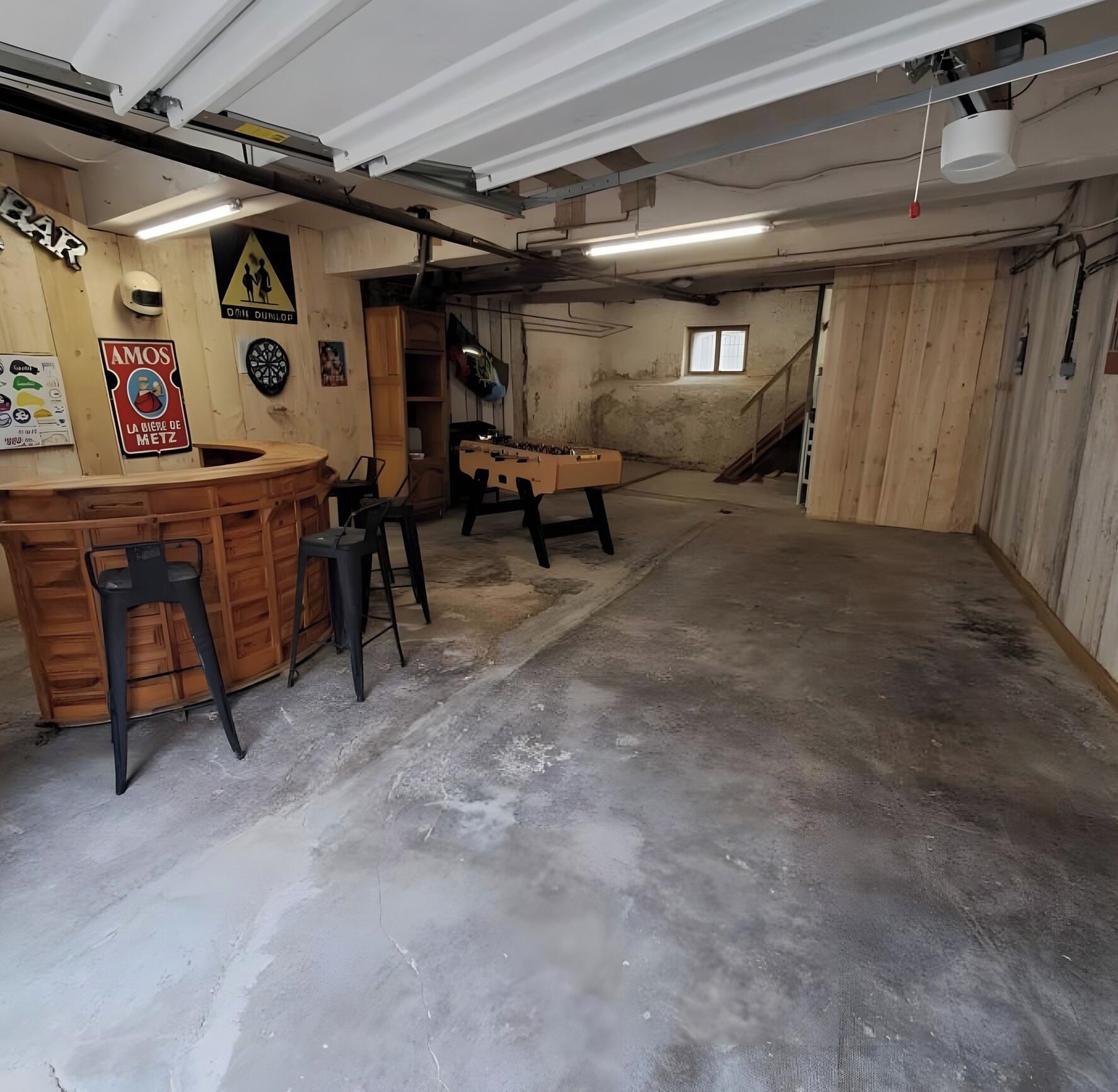 Un sous-sol aménagé avec un coin bar, des chaises, une table de baby-foot et un jeu de fléchettes.