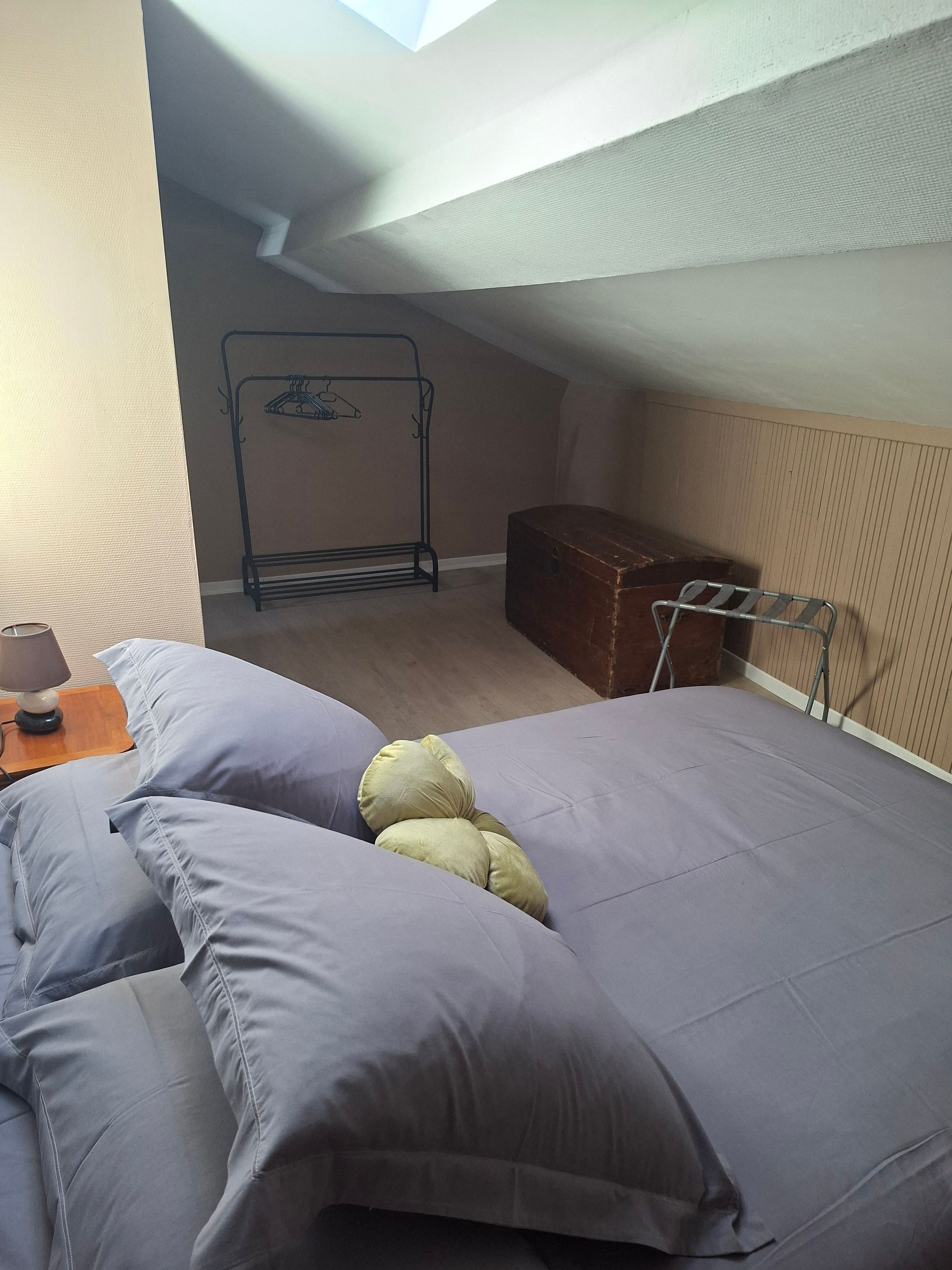 Une pièce comprenant un lit, une table de chevet, une lampe, un étendoir à linge en métal et une commode en bois.