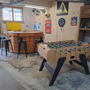 A room with a foosball table, bar area, and dartboard.