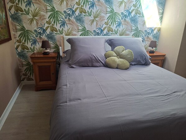 Quarto com cama, duas mesas de cabeceira, abajur e papel de parede floral.