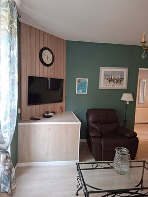 Un salon équipé d’un téléviseur à écran plat, d’un comptoir d’accueil en bois, d’un canapé en cuir marron, d’une table basse en verre et d’un tableau encadré accroché au mur.