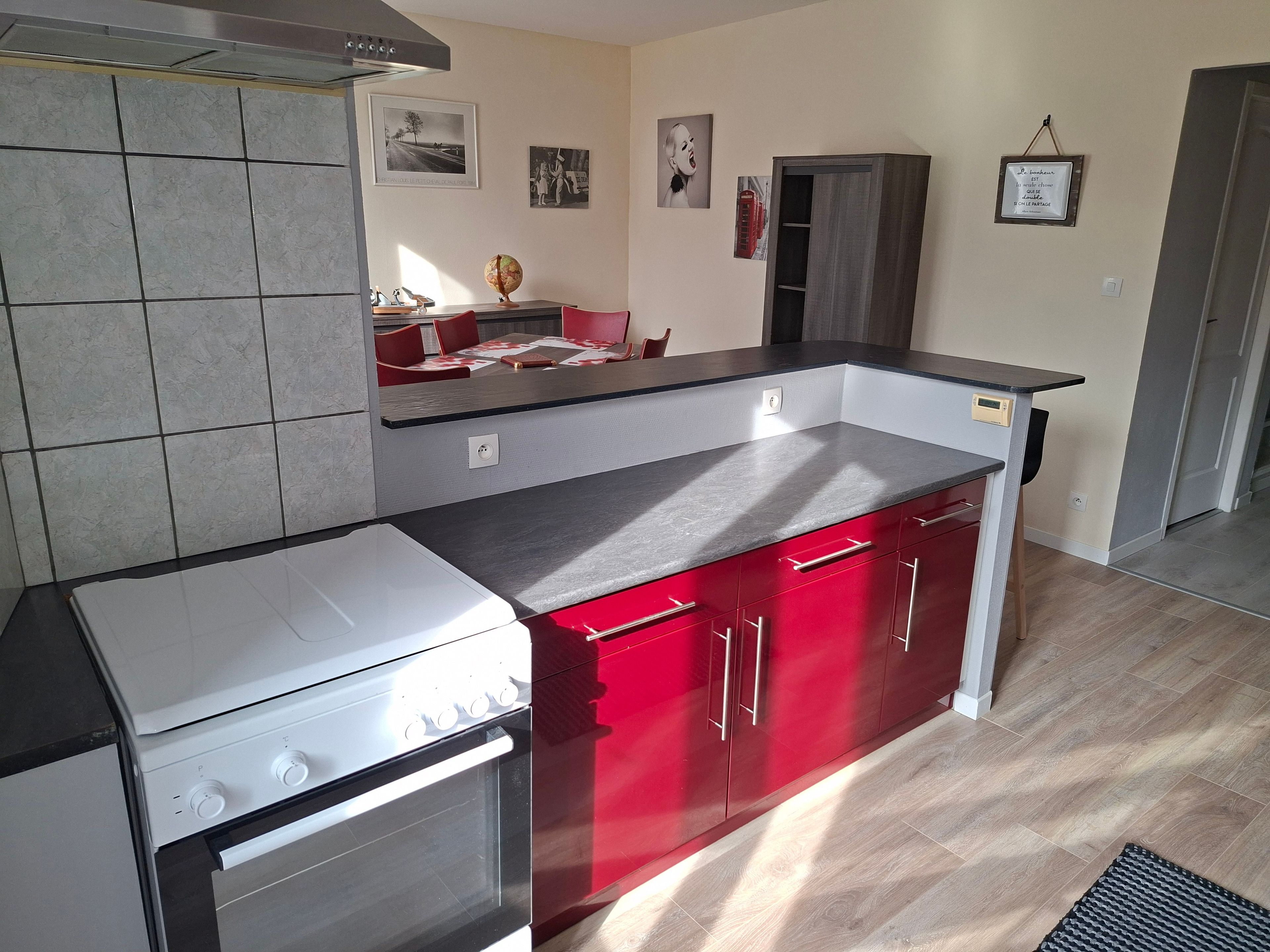 Eine Küche mit Herd, Backofen und roten Schränken. Es gibt einen Essbereich mit Tisch und Stühlen.