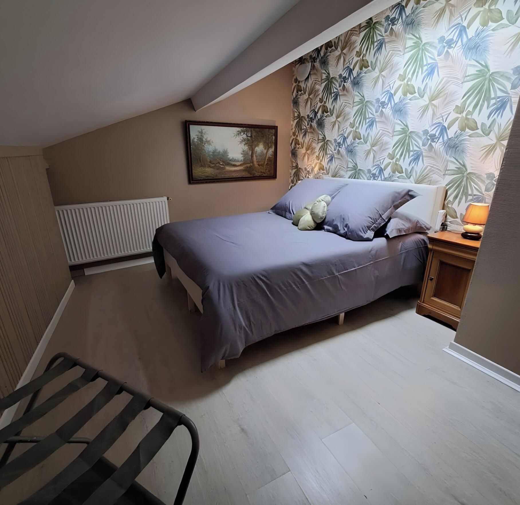 Une chambre à coucher avec un lit, un radiateur, un tableau, une table de chevet avec une lampe et une chaise.