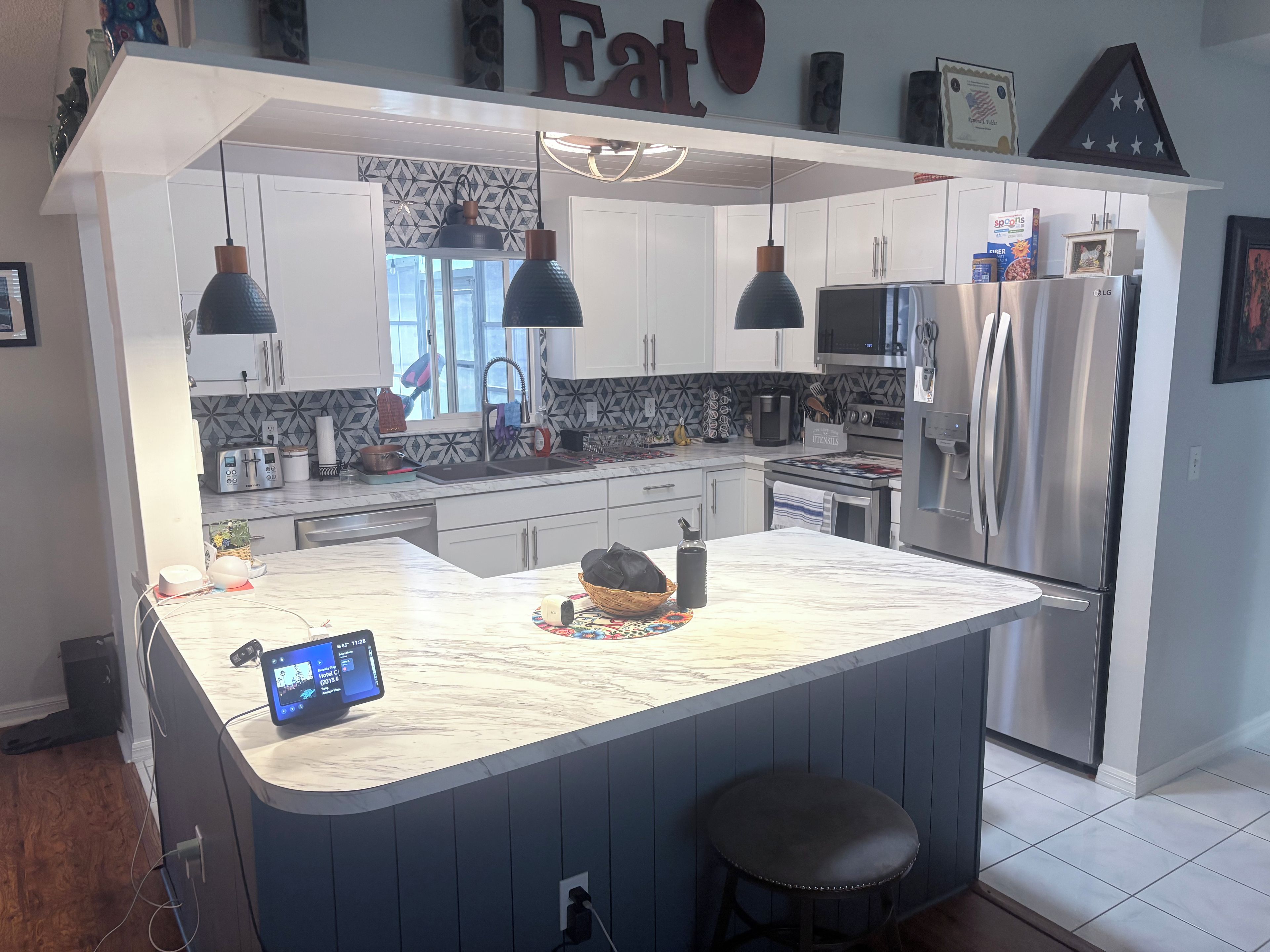 A modern kitchen with a central island, stainless steel appliances, pendant lighting, and a digital clock.