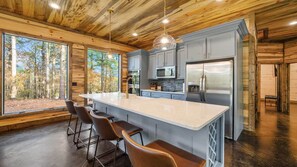 A modern kitchen with a large island, bar stools, and a view of the forest. - Starfire Baby corn cabins (Hochatown)