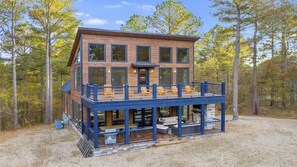 A two-story wooden cabin with a balcony, surrounded by trees. - Starfire Baby corn cabins (Hochatown)
