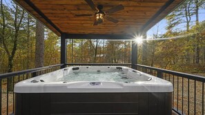 Ein Whirlpool unter einer Holzterrasse mit Deckenventilator, umgeben von Bäumen.