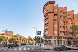 Edifício de vários andares com fachada curva, diversas varandas e vista para a rua com carros e pedestres.