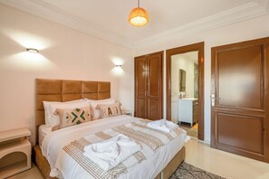 Un dormitorio con cama, mesita de noche, armario y baño visible a través de una puerta abierta.