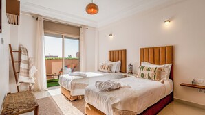 Ein Hotelzimmer mit zwei Betten, einem Balkon, einem Holzstuhl und einer Pendelleuchte.