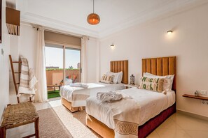 Habitación de hotel con dos camas, un balcón, una silla de madera y una lámpara colgante.