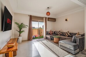 Uma sala de estar moderna com um sofá cinza, uma mesinha de madeira, uma planta em vaso e uma televisão de tela plana fixada na parede.