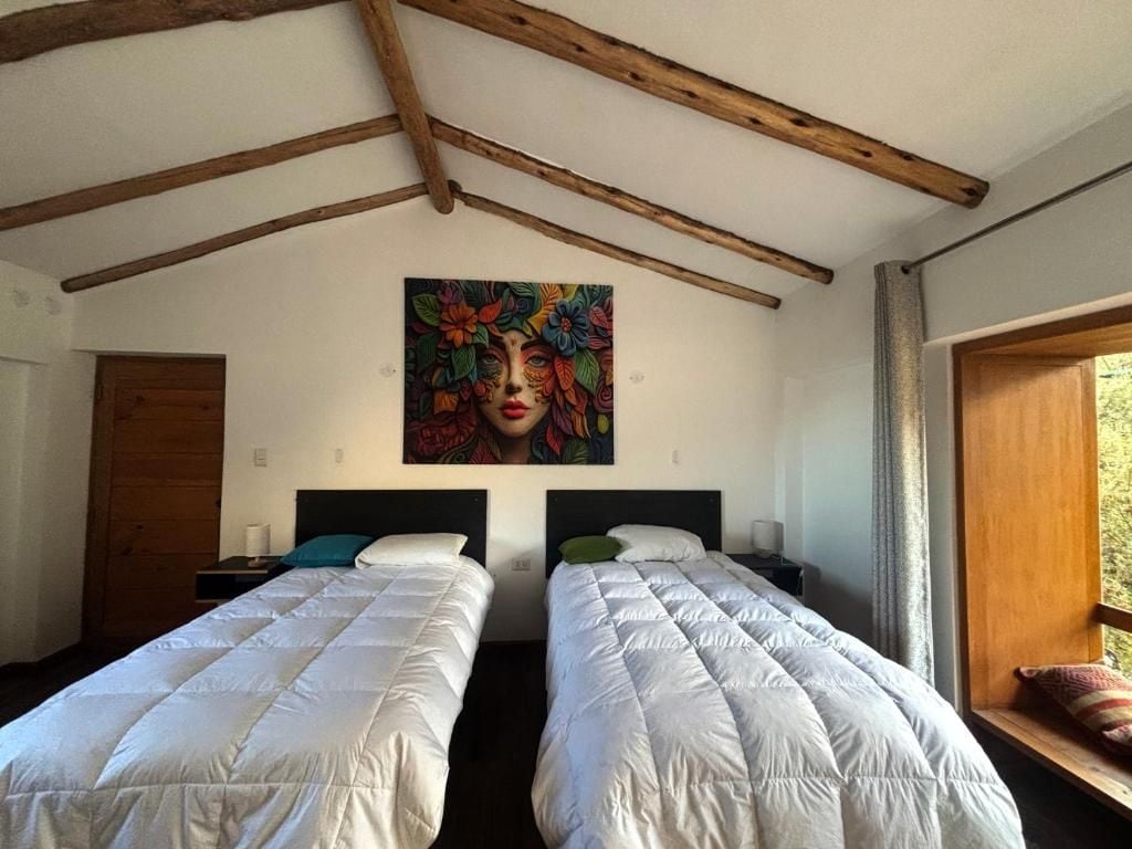 Een kamer met twee bedden, houten balken in het plafond, een schilderij aan de muur en een raam met gordijnen.