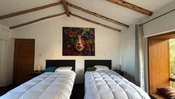 Een kamer met twee bedden, houten balken in het plafond, een schilderij aan de muur en een raam met gordijnen.